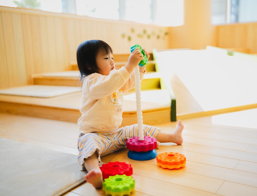 木のフロアでおもちゃを重ねて遊ぶ子ども